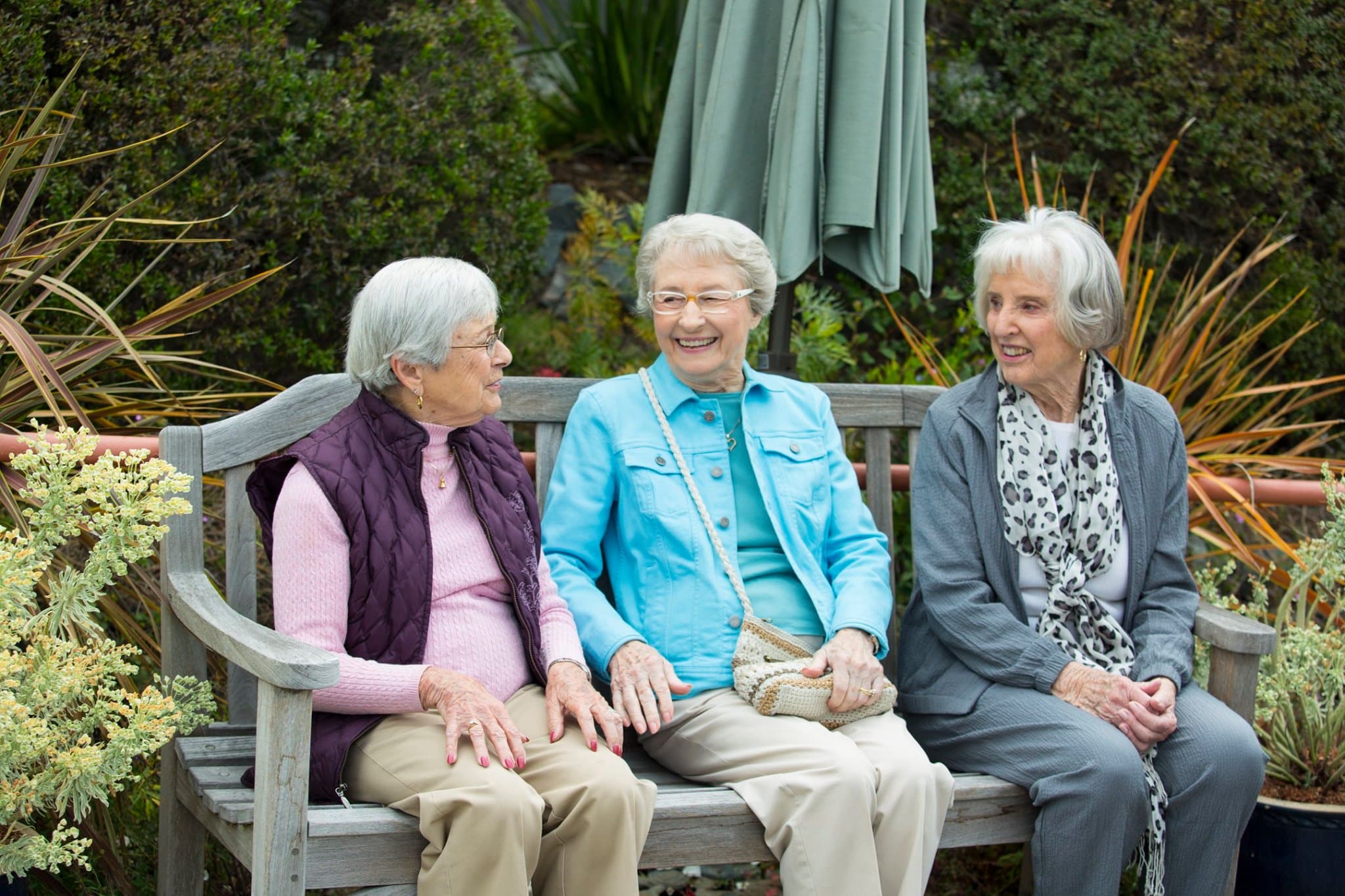 Three older people sitting on a bench outside smiling